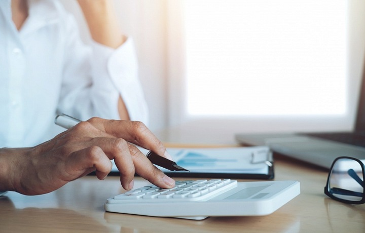 Ruka držící pero a kalkulačka.