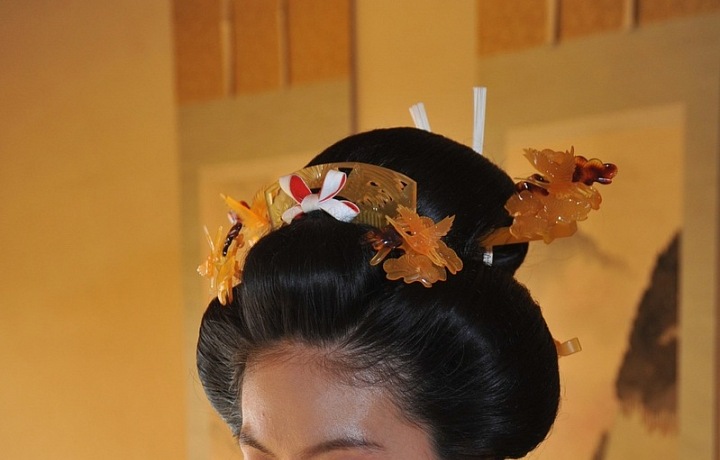 Vlasy má upraveny do tradičního komplikovaného účesu ozdobeného hřebínky a jinými doplňky