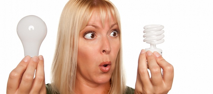 Žena držící dvě žárovky - normální a úspornou