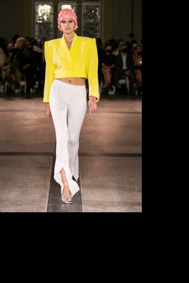 Modelka má na sobě žlutý kabátek a bílé kalhoty od Vandy Jandy