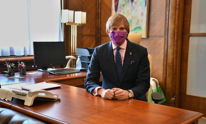 Adam Vojtěch sedí v roušce za pracovním stolem.