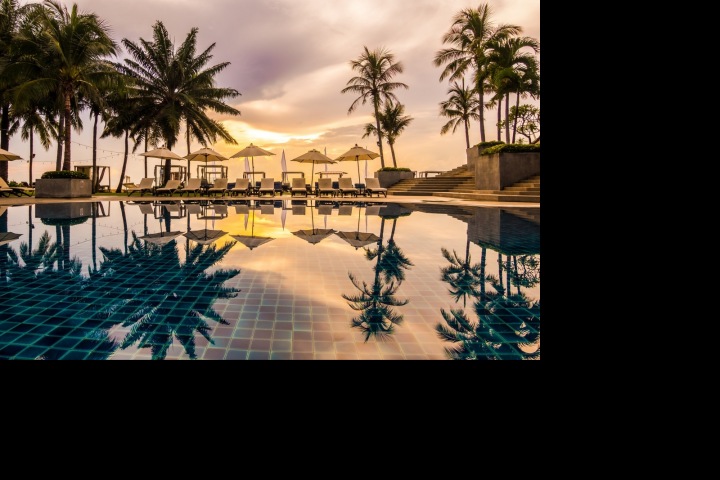 Nádherný hotel s bazénem a palmami při západu slunce.