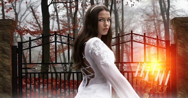 Dívka ve svatebním se svícnem před branami hřbitova