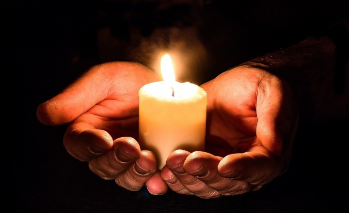 Člověk držící zapálenou svíčku v dlaních.