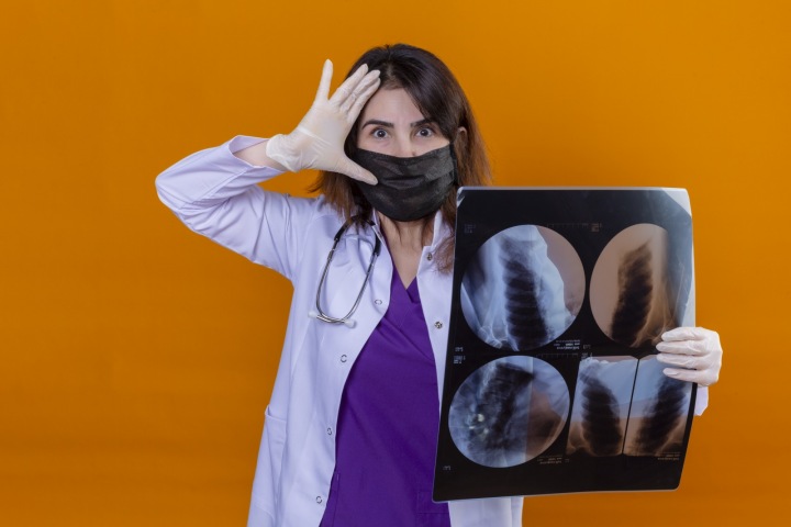 Lékařka v roušce analyzující rentgen plic