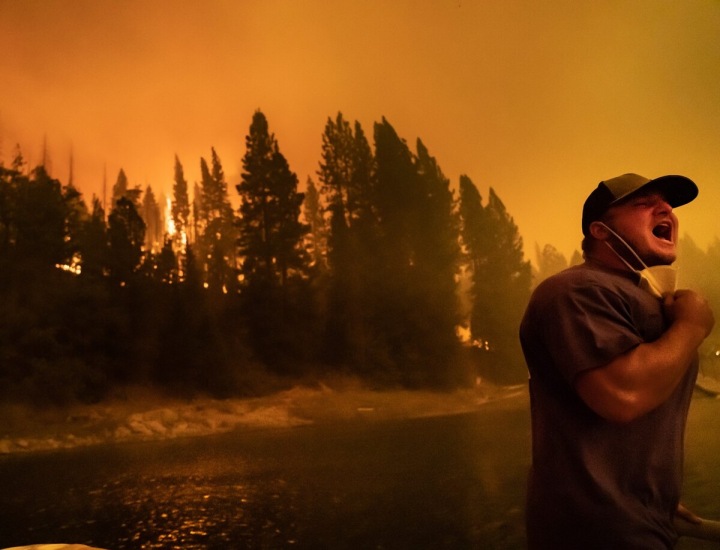 Na fotografii stojí křičící muž, v pozadí řádí požár