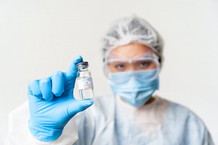 Žena v ochranném oděvu držící vakcínu Žena v ochranném oděvu držící vakcínu