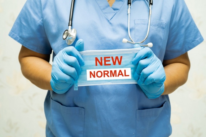 Mužské ruce držící masku s nápisem "Nová normalita" Mužské ruce držící masku s nápisem "Nová normalita"