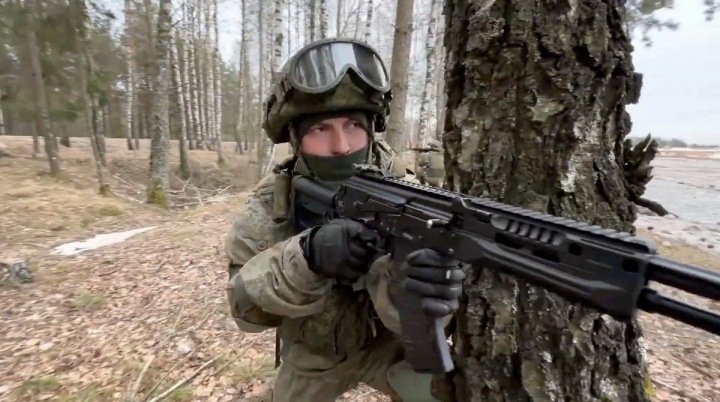 Voják se zbraní za stromem.