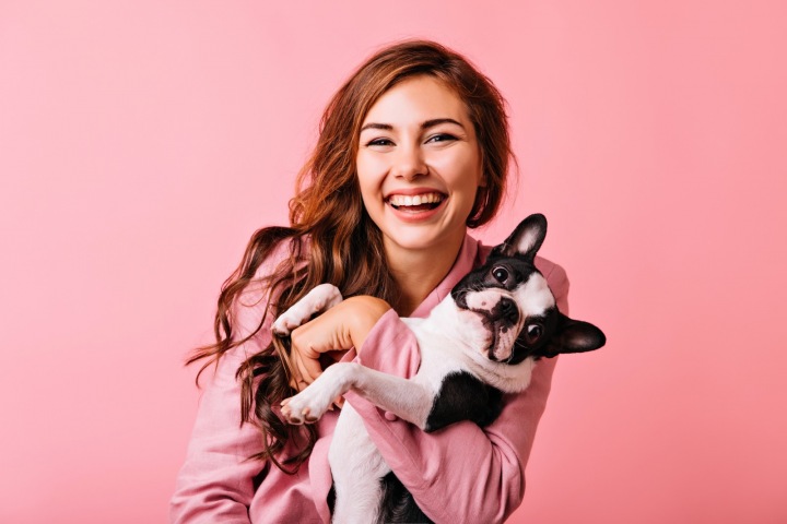 Rozesmátá dlouhovlasá dívka s psím mazlíčkem v náručí