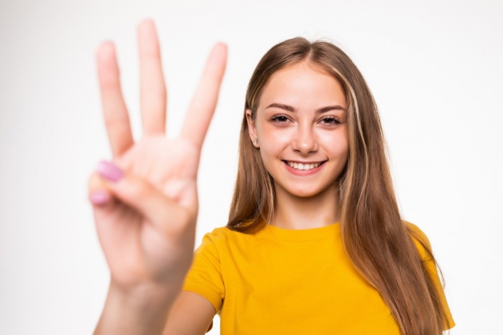Usmívající se dívka ukazuje na prstech číslo 3 Usmívající se dívka ukazuje na prstech číslo 3