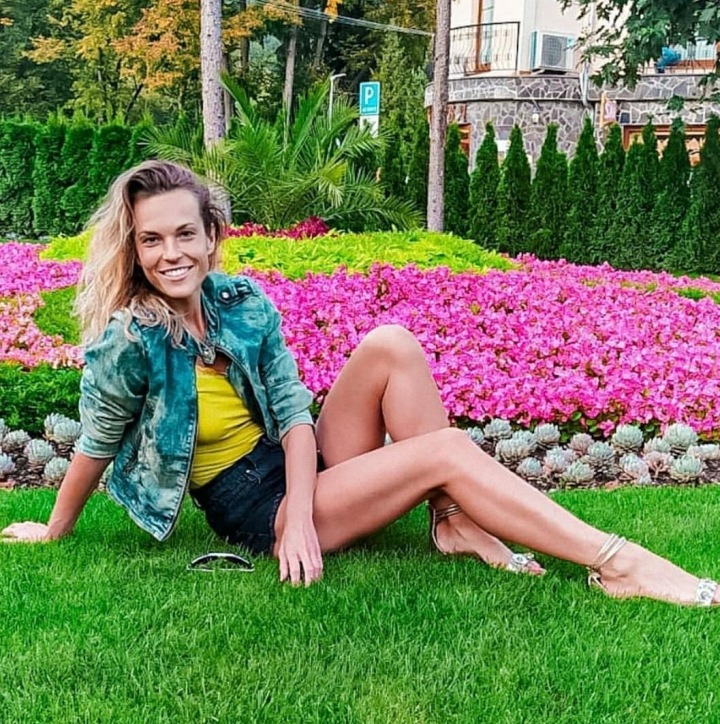 Usmívající se mladá žena sedící na zemi před barevným záhonem