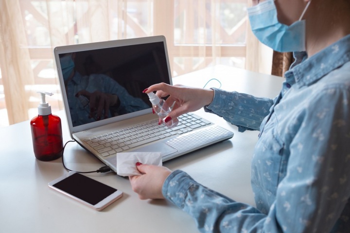 Žena s rouškou si dezinfikuje notebook Žena s rouškou si dezinfikuje notebook