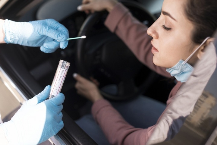 Žena sedí v autě a je jí prováděn test na covid-19 Žena sedí v autě a je jí prováděn test na covid-19