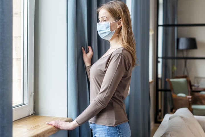 Žena s rouškou se dívá z okna Žena s rouškou se dívá z okna