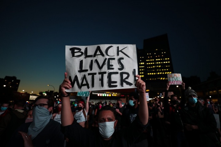 Žena v roušce drží nad hlavou plakát Black lives matter Žena v roušce drží nad hlavou plakát Black lives matter