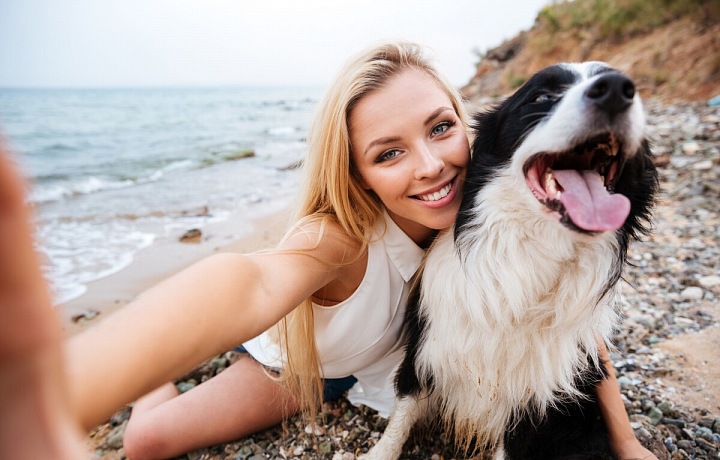 Usměvavá dívka na pláži dělající si selfie se svým psem
