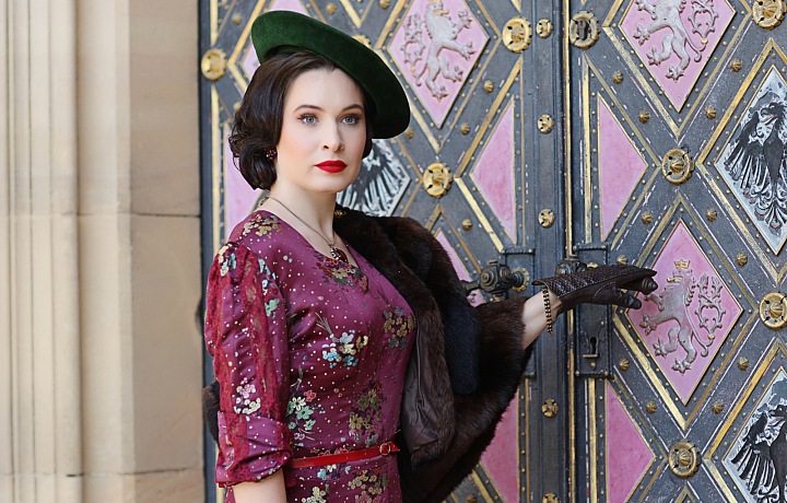 Dívka v šatech ve stylu první republiky před dekorativními dveřmi