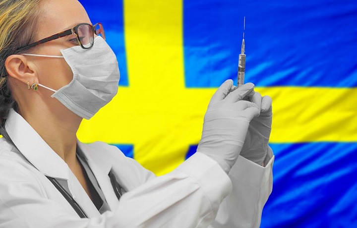 Lékařka s injekční stříkačkou v pozadí se švédskou vlajkou