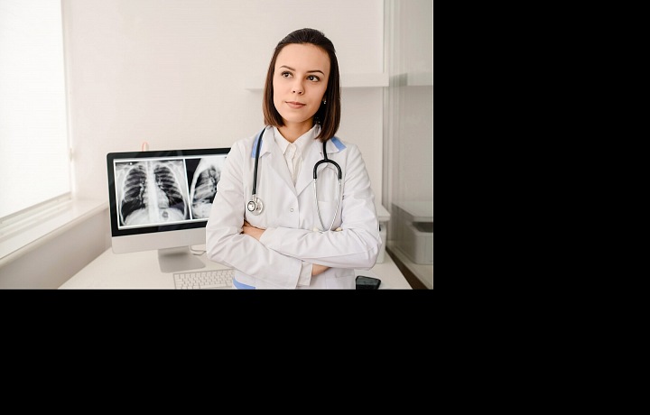 Lékařka v nemocnici s rentgenovým snímkem na obrazovce počítače v pozadí.