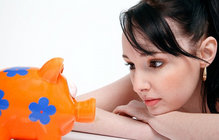 Mladá žena se dívá na oranžovou kasičku.