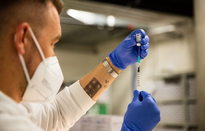 Muž s respirátorem nabírá vakcínu do injekční stříkačky