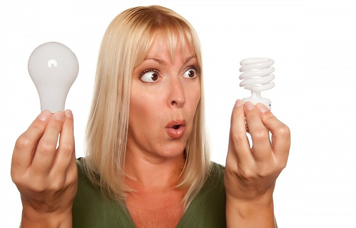Žena držící dvě žárovky - normální a úspornou