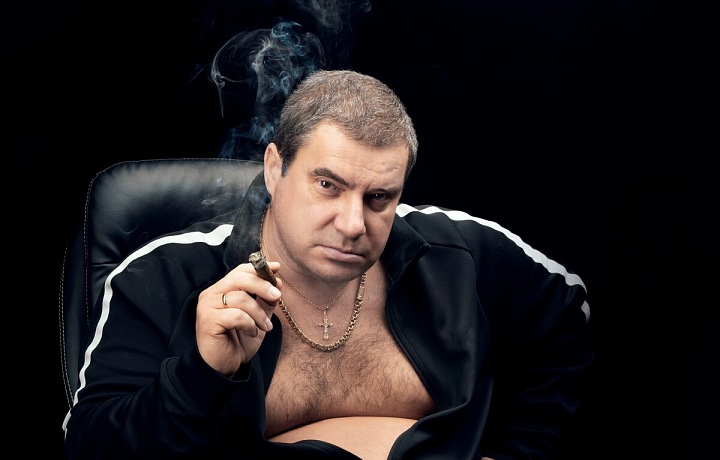 Muž sedí ve sportovní mikině v křesle a kouří doutník
