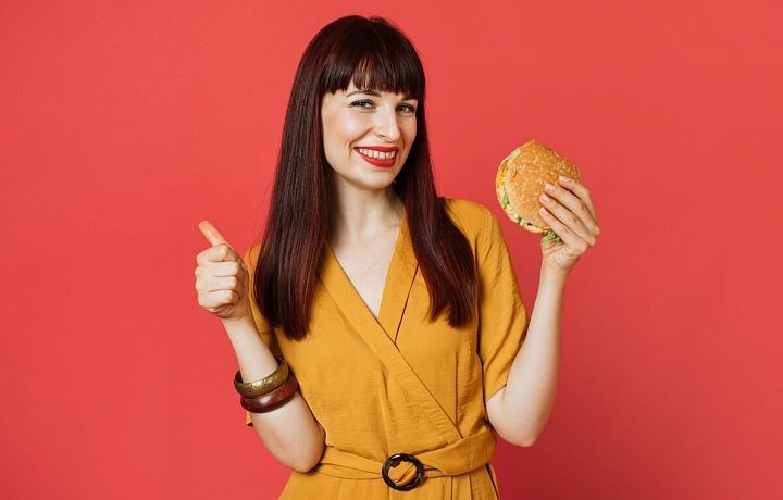 Žena s haburgerem v ruce na červeném pozadí